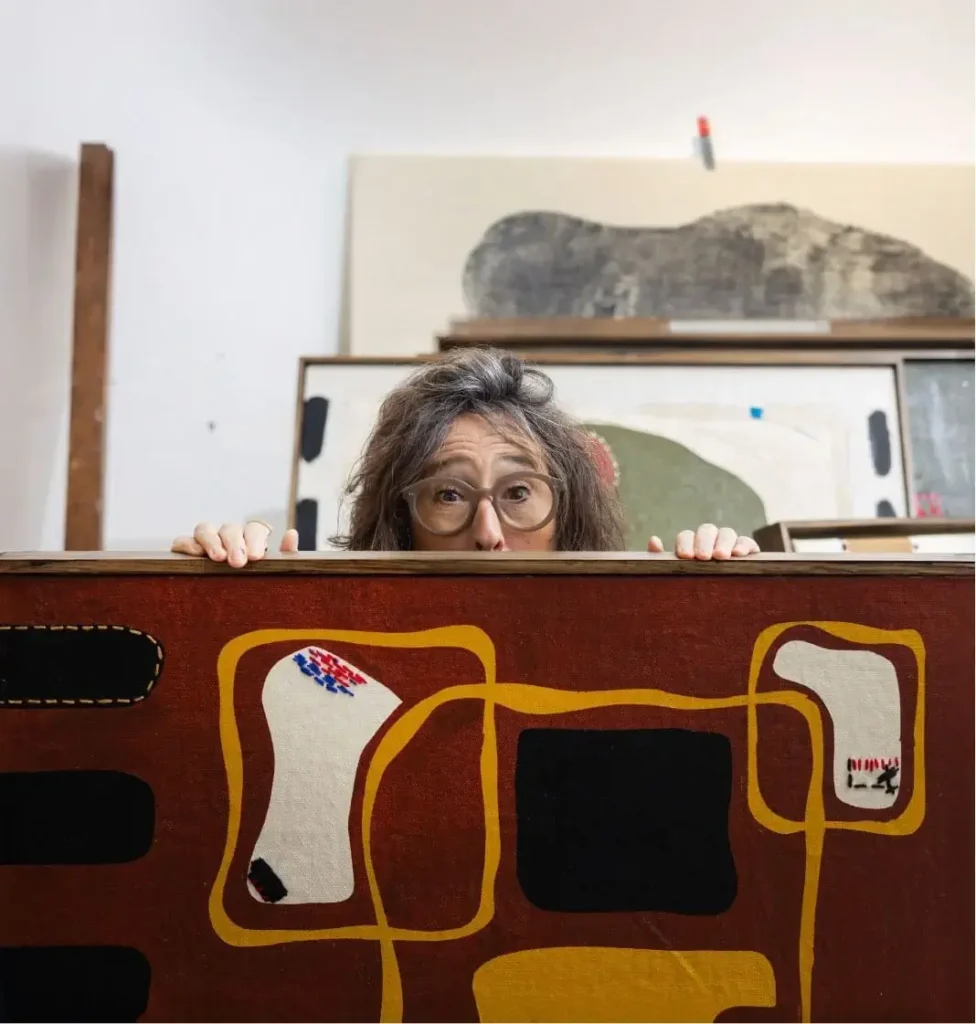 Una persona amb ulleres mira una gran pintura abstracta amb formes i colors atrevits en un estudi d'art.